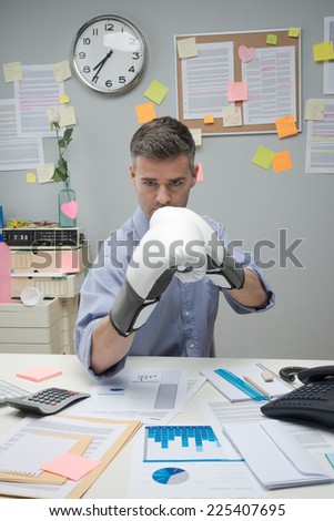 Businessman at workplace wearing boxing gloves in guard position.