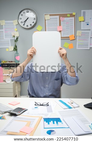 Office worker hiding behind a white blank sign in a small office.