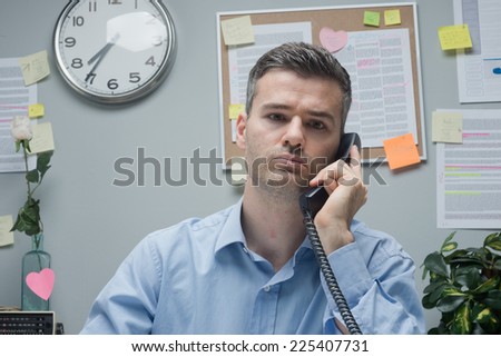 Pensive white collar on the phone sitting at office desk.