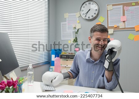 Cheerful businessman calling and wearing boxing gloves at workplace.