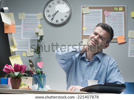 Tired businessman sitting at desk touching his painful neck.