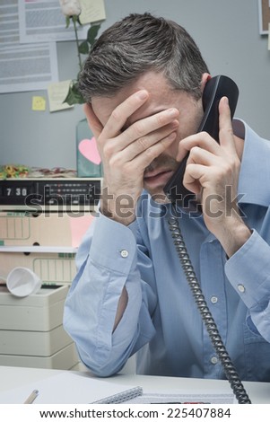 Stressed employee on the phone touching his forehead.