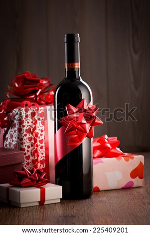 Wine bottle gift with red ribbon and colorful christmas gift boxes on wooden table.