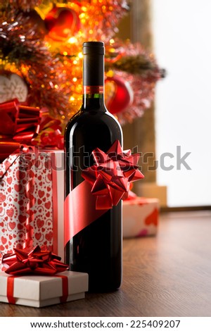 Wine bottle with red ribbon with christmas gift boxes and tree on background.