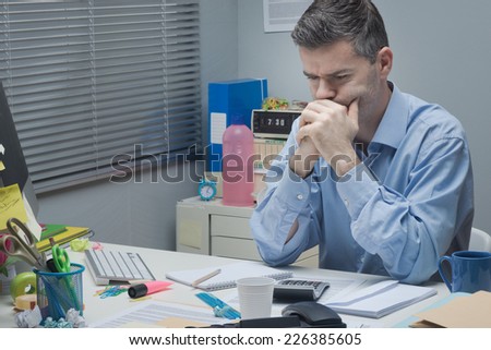 Pensive businessman at desk with hands clasped looking down.