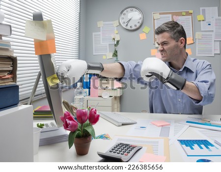 Mad angry office worker punching computer with boxing gloves.