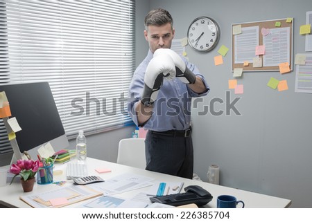 Businessman at workplace wearing boxing gloves in guard position.