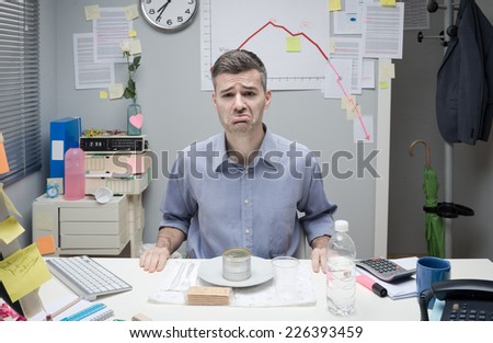 Sad businessman having lunch with canned food and negative business chart on background.