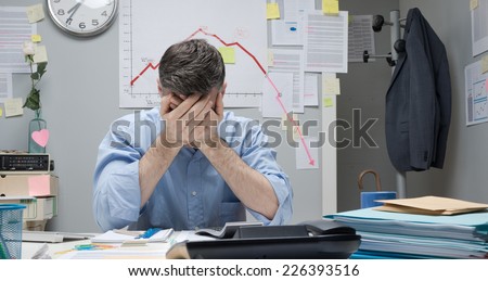 Desperate office worker with head in hands and negative financial chart on background.