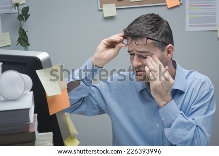 Office worker with eye pain touching his eyes and holding glasses.