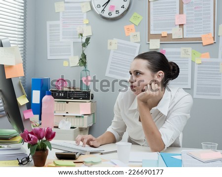 Bored frustrated female office worker working at computer with hand on chin.
