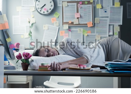 Tired businesswoman sleeping in office overnight with pillow on desk.