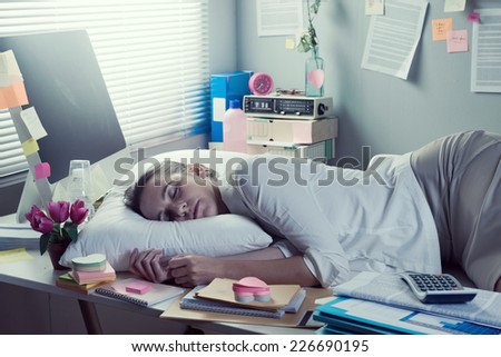 Tired businesswoman sleeping in office overnight with pillow on desk.