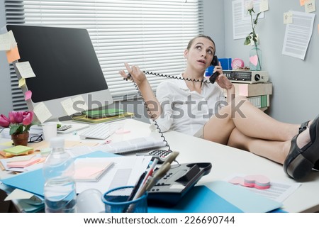Smiling lazy woman feet up on desk talking on the phone.