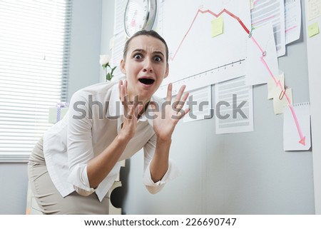 Shocked businesswoman mouth open checking a negative business chart on office wall.