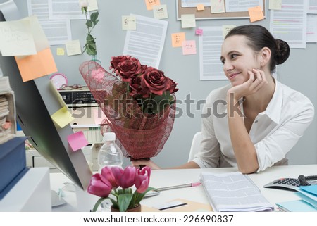 Young smiling woman receiving romantic red roses bouquet at office.