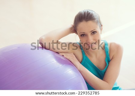 Attractive smiling woman exercising at gym with fitness ball, sitting on the floor.