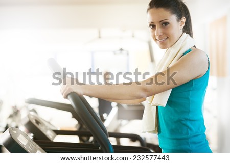Attractive young woman smiling and doing cardio exercise on treadmill at gym.