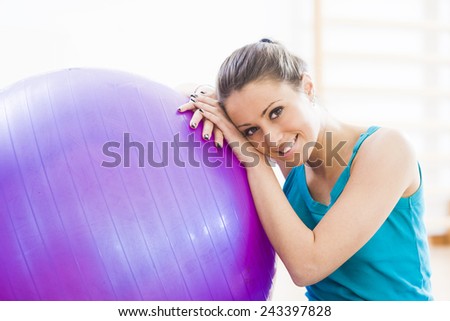 Attractive smiling woman exercising at gym with fitness ball, sitting on the floor.