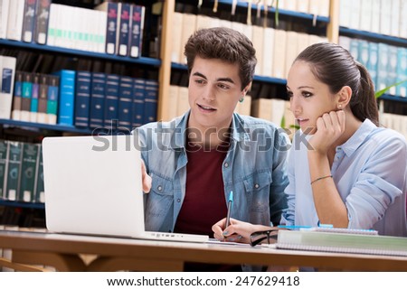 Young students studying together at the library with white laptop