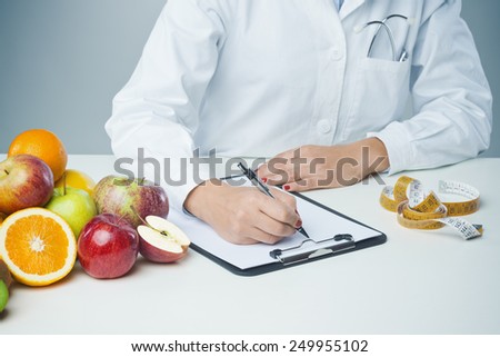 Female nutritionist at work writing documents on a clipboard with fresh fruit on foreground