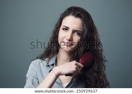 Sad young woman brushing her tangled  frizzy hair