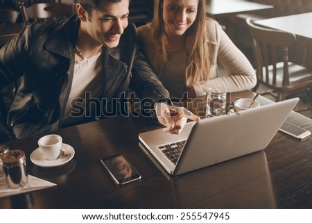 Cheerful couple at the cafe with a computer, he is pointing at the laptop screen