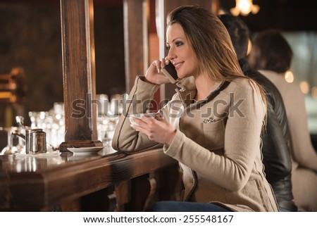 Beautiful girl sitting at the bar counter and having a phone call with her mobile phone