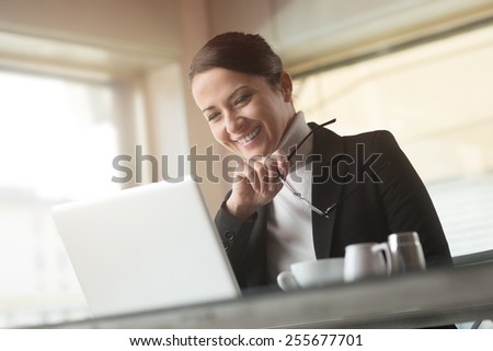 Smiling young businesswoman at the bar working on her laptop