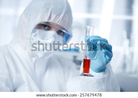 Researcher in hazmat protective suit examining a test tube in the chemical lab.