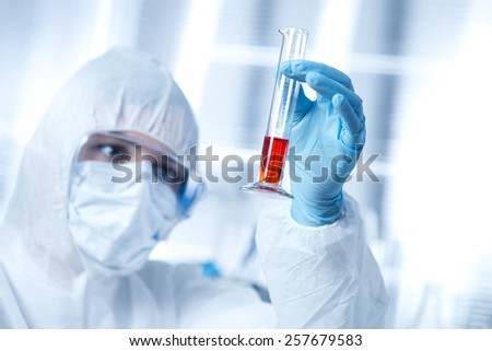 Researcher in hazmat protective suit examining a test tube in the chemical lab.