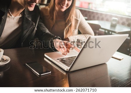 Cheerful couple at the cafe with a computer, he is pointing at the laptop screen