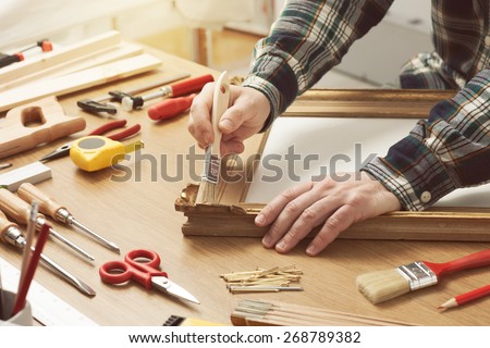 Man varnishing a wooden frame hands close up with DIY tools on a work table