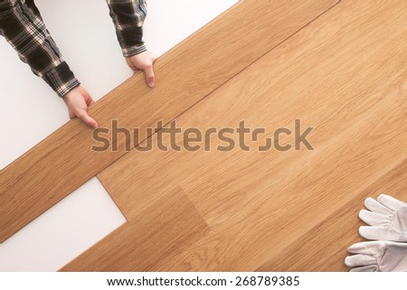 Top quality wooden floor installation at home, carpenter\'s hands placing a tile on the floor top view