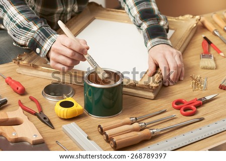 Decorator varnishing a wooden frame hands close up with DIY tools, hobby and craft concept