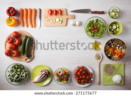 Healthy eating concept with fresh vegetables and salad bowls on kitchen wooden worktop, copy space at center, top view