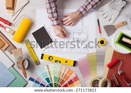 Professional decorator drawing on a house project with work tools, painting rollers and color swatches all around, top view
