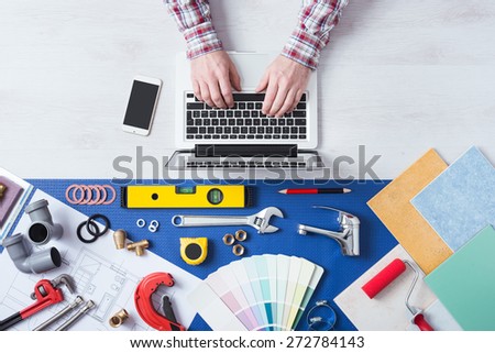 Male hands using a laptop next to plumbing work tools, tiles and swatches, online booking and home plumber service
