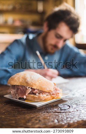 Tasty sandwich with ham and fresh bread with young man sitting at kitchen table and sketching