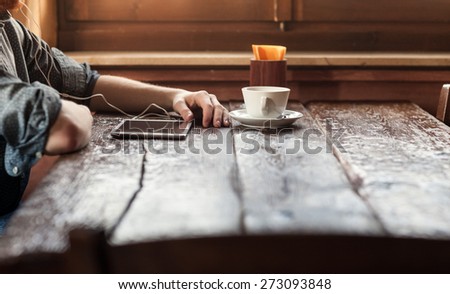 Young man having a coffee break at the bar and listening to music with his tablet using earphones