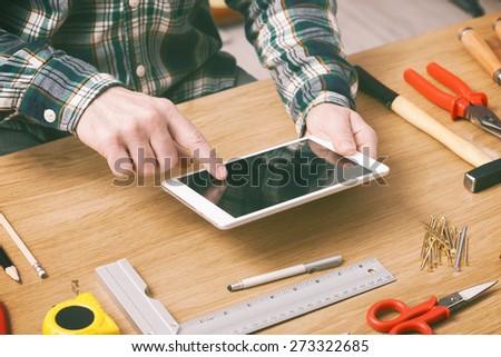 Man working on a DIY project at home with a digital tablet, carpentry and construction tools on a work table, hands close up