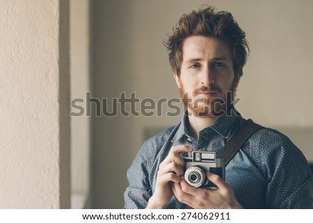 Vintage hipster photographer portrait, he is holding an old camera and posing