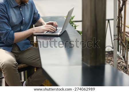 Unrecognizable man using a modern portable computer on an outdoor table, street on background