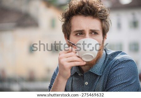 Hipster guy having a cappuccino at the bar, he is pensive and looking away