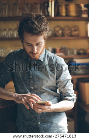 Young hipster man using his mobile phone and leaning on a bar counter