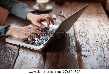 Man working on a laptop on a rustic wooden table, hands close up