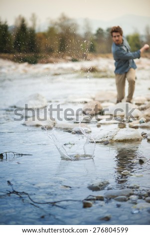 Young man throwing stones in the river and water splash, nature and freedom concept