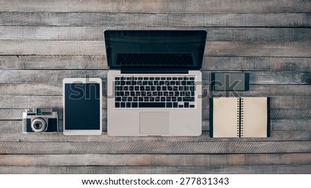 Grunge hipster wooden desktop with computer, digital tablet, vintage camera, smart phone and notebook, top view