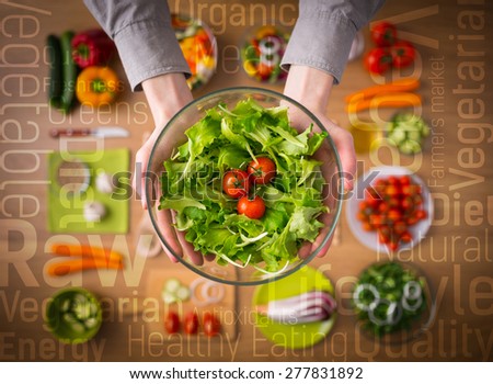 Hands holding an healthy fresh vegetarian salad in a bowl, fresh raw vegetables on background and healthy eating text concepts