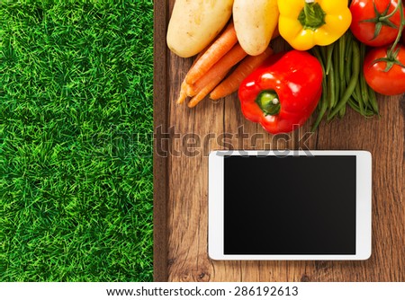 Touch screen digital tablet, fresh vegetables and grass on a wooden table, food and gardening app concept